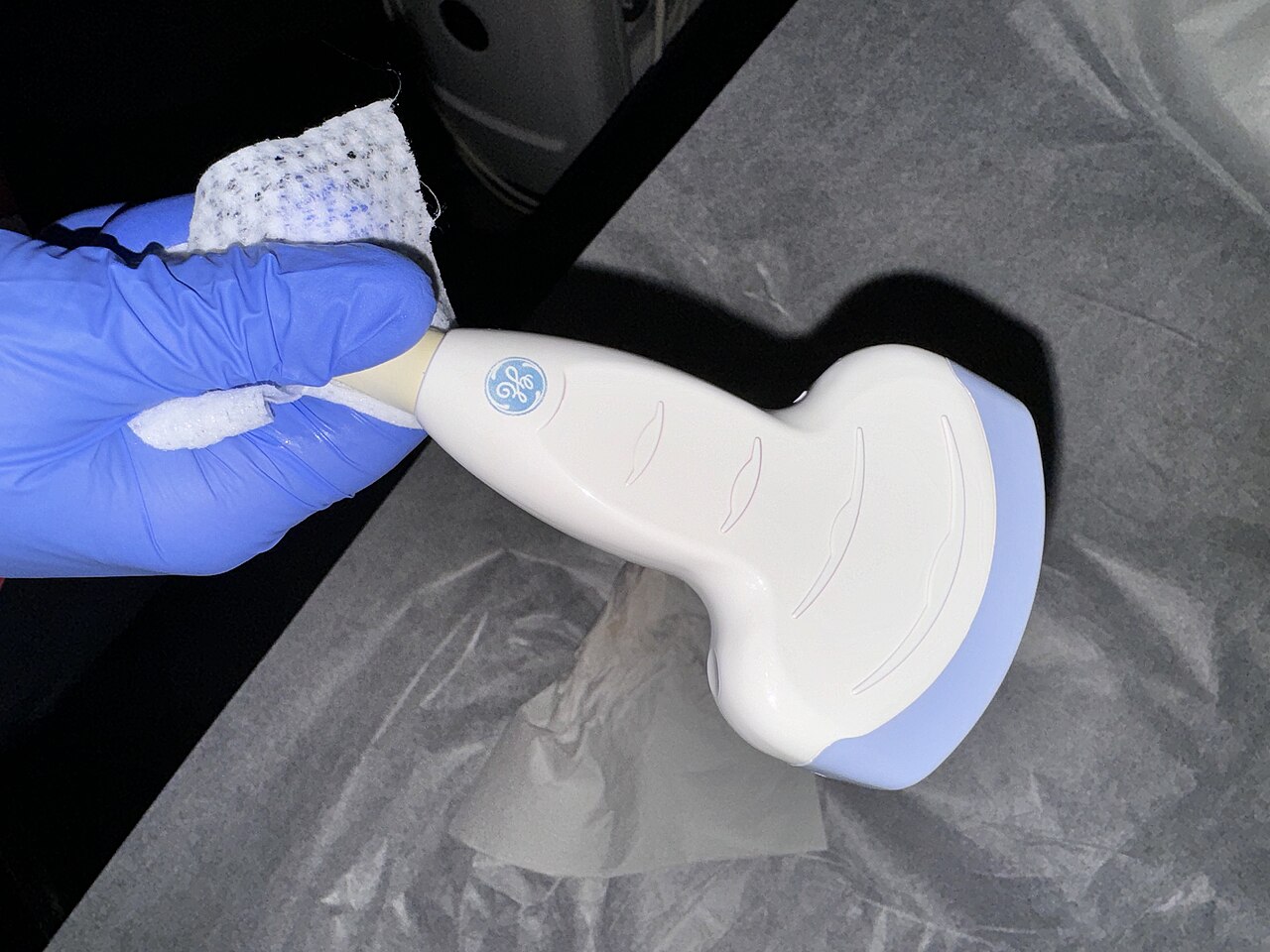 A handheld ultrasound linear-array probe, the scan head held in a gloved hand