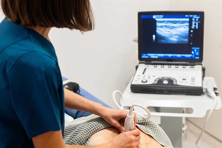 An operator works a convex ultrasound probe on a patient's upper abdomen, watching the screen.