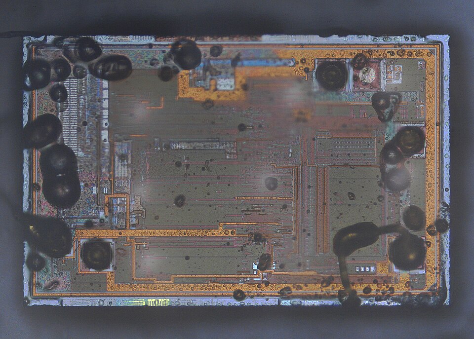 A decapped microcontroller die under magnification, bond wires ringing the silicon around its logic and memory blocks.