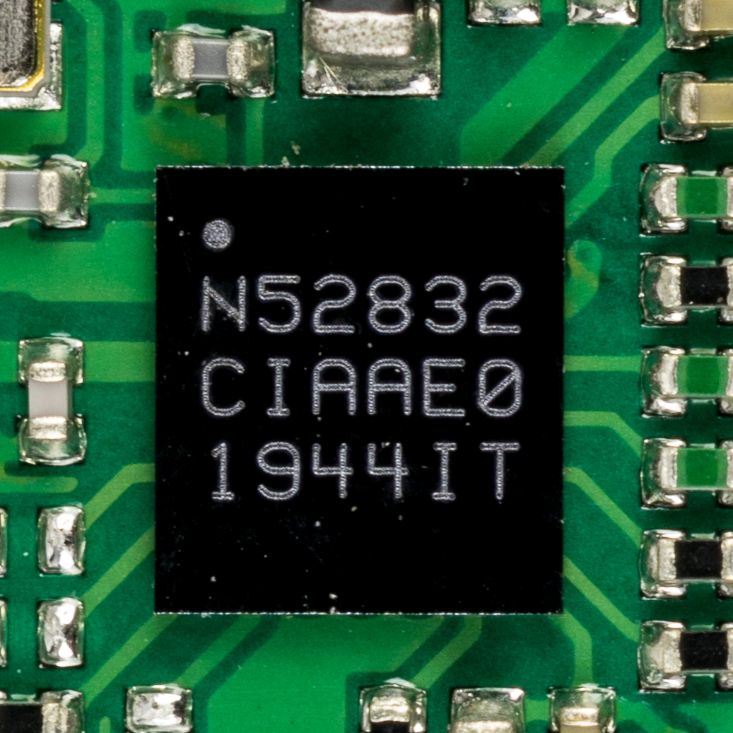 A Nordic Semiconductor nRF52832 microcontroller in a QFN package soldered onto a green circuit board, its part marking N52832 visible, surrounded by small passive components.