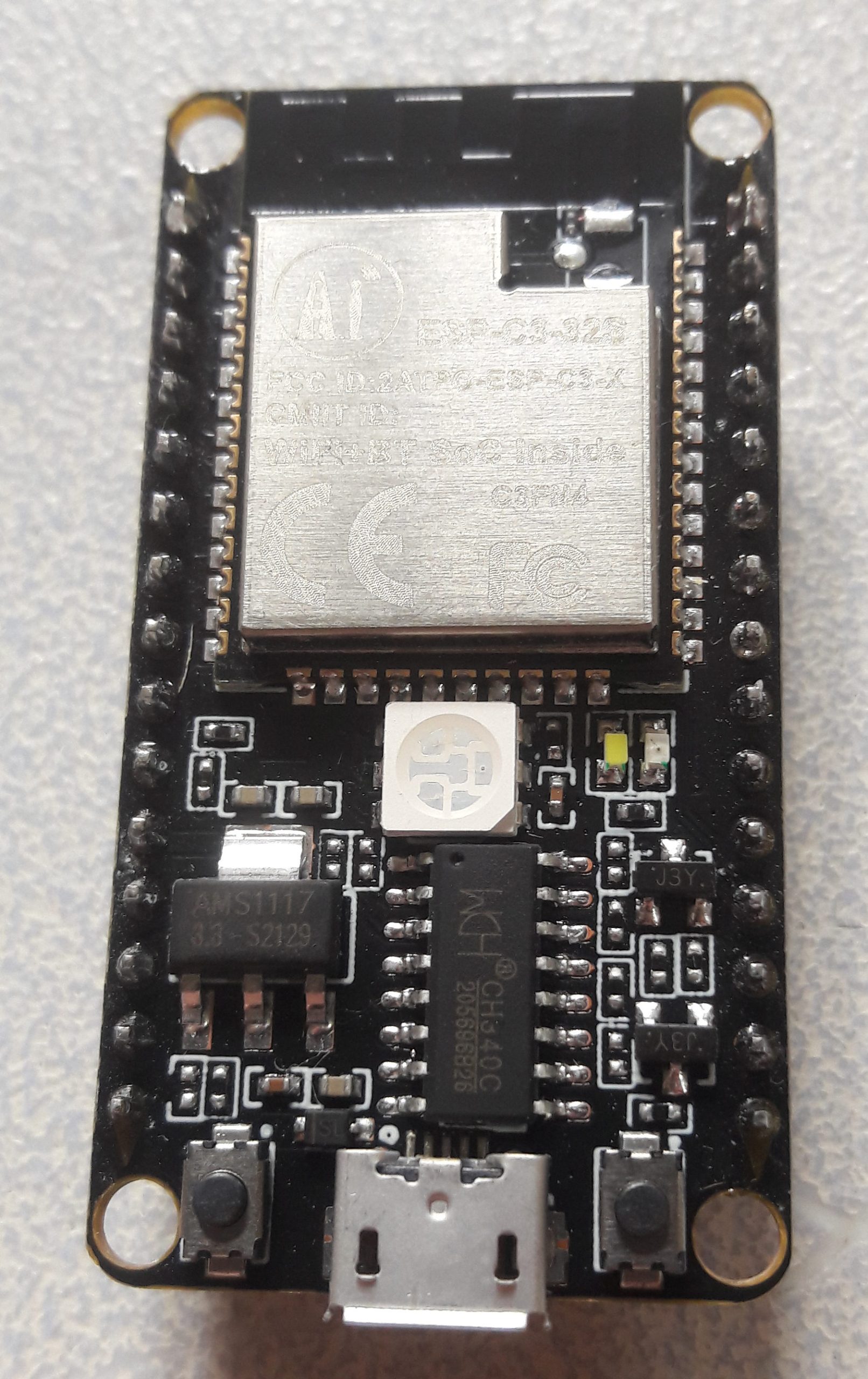 A black ESP32-C3 development board with a metal-shielded Espressif radio module, a USB-serial chip, voltage regulator, RGB LED and micro-USB connector, gold castellated pin headers down both sides.