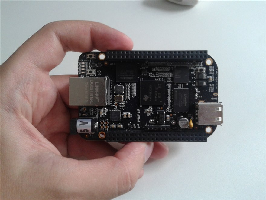 A BeagleBone Black single-board computer held in a hand, the TI Sitara AM335x processor, Ethernet, HDMI and USB visible on the black PCB.