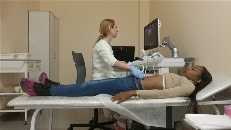 A clinician performs an abdominal ultrasound on a patient lying on an examination couch, watching the screen.