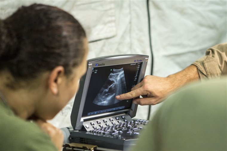 A clinician reviews a portable ultrasound screen showing an abdominal image during a focused point-of-care exam.