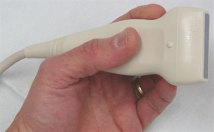 A handheld ultrasound probe held in the hand, its cable running off toward the connector that plugs into the base.