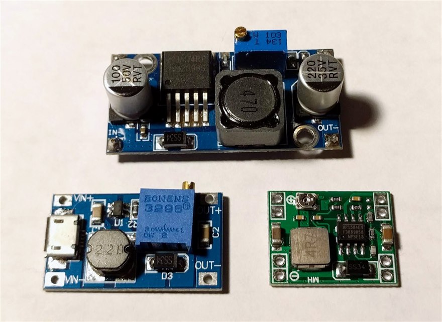 Three small switching DC-DC converter modules, an LM2596 step-down, a boost module and an MP1584 step-down, each with its regulator IC, inductor and electrolytic capacitors.