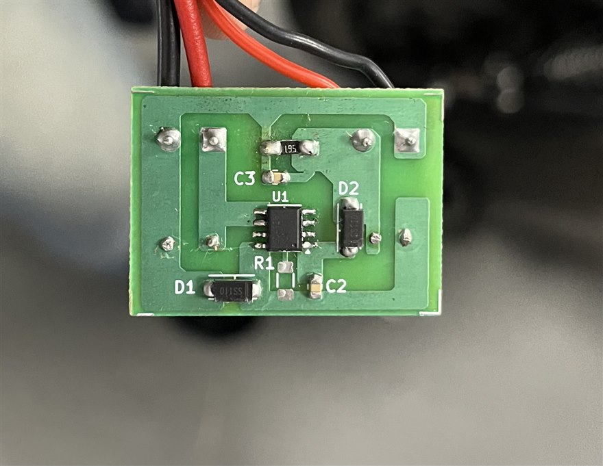 A small switching regulator board with a SOT-23 controller IC, a catch diode and its capacitors, fed by input and output wires.