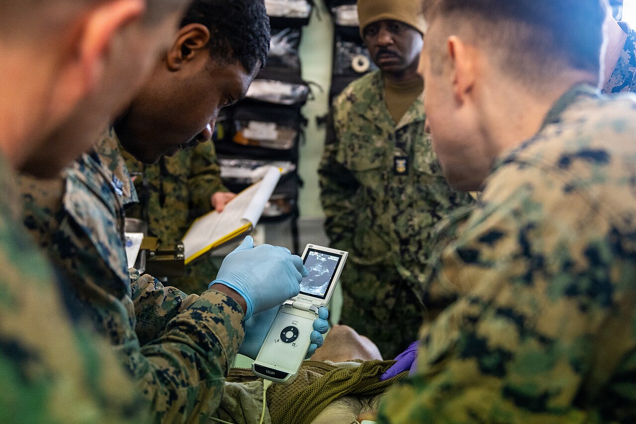 A clinician using a handheld ultrasound at the bedside, the scanner held in one hand