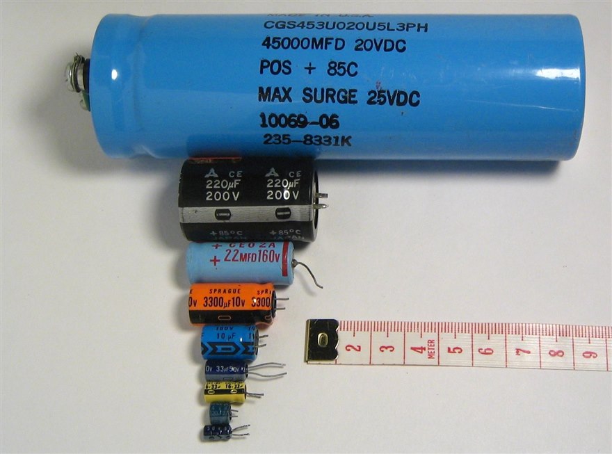 Cylindrical aluminum electrolytic capacitors from a large 45000 microfarad can down to small radial parts, with a ruler for scale.
