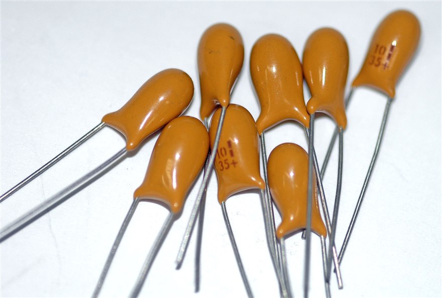 A group of orange teardrop-shaped radial-leaded tantalum capacitors marked with their value and voltage.