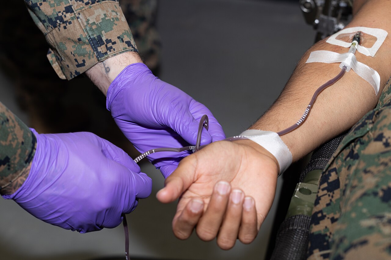An intravenous line taped into a forearm at the elbow in a field setting