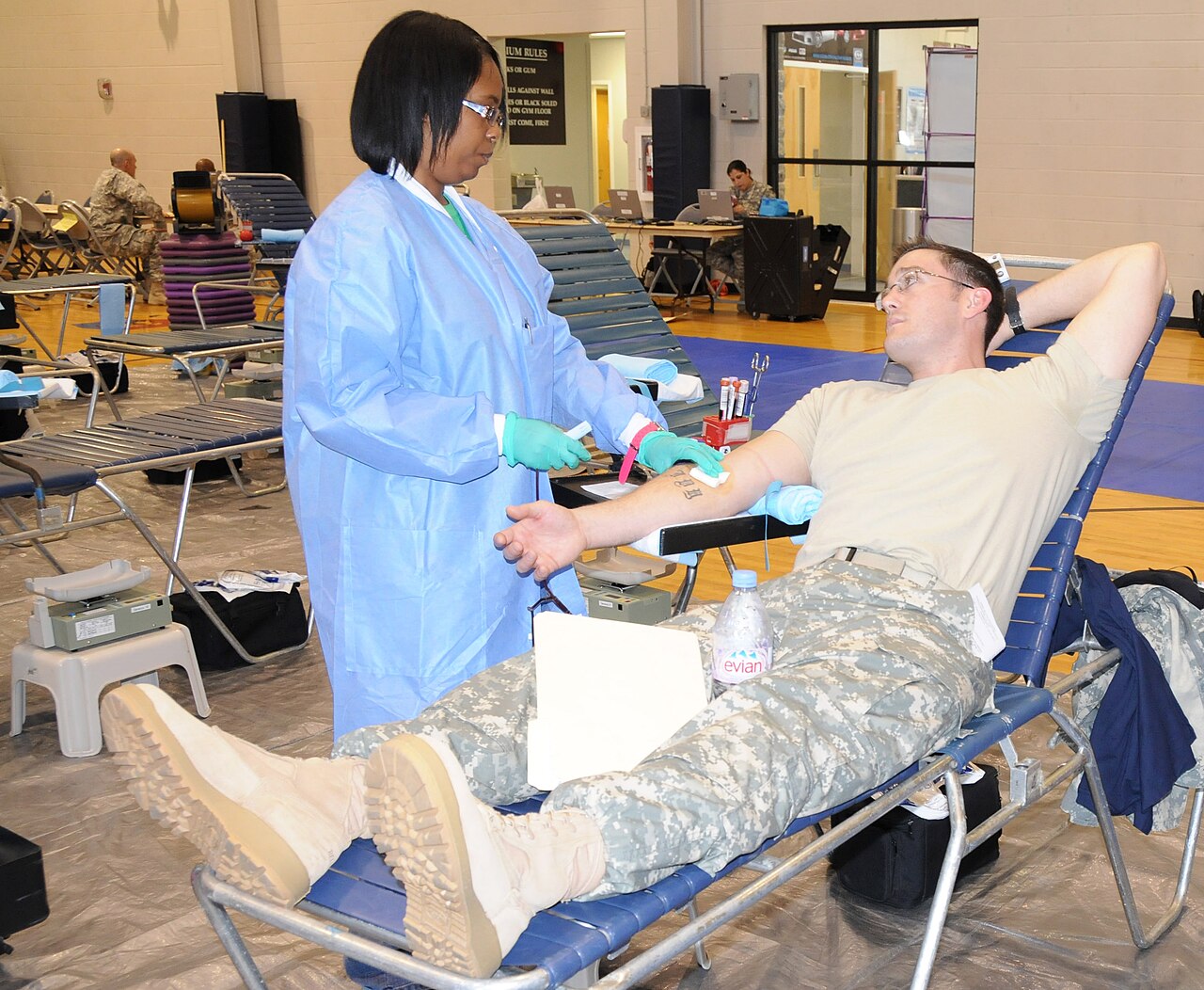 A gloved clinician drawing blood from the arm of a seated person