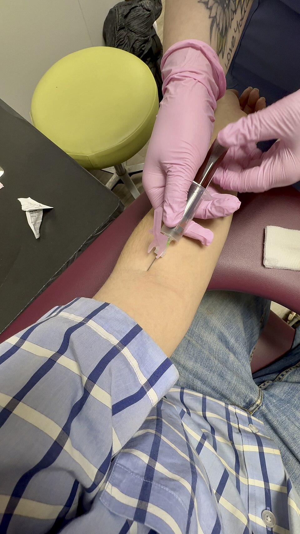 A clinician in gloves drawing blood from a vein at the bend of the elbow