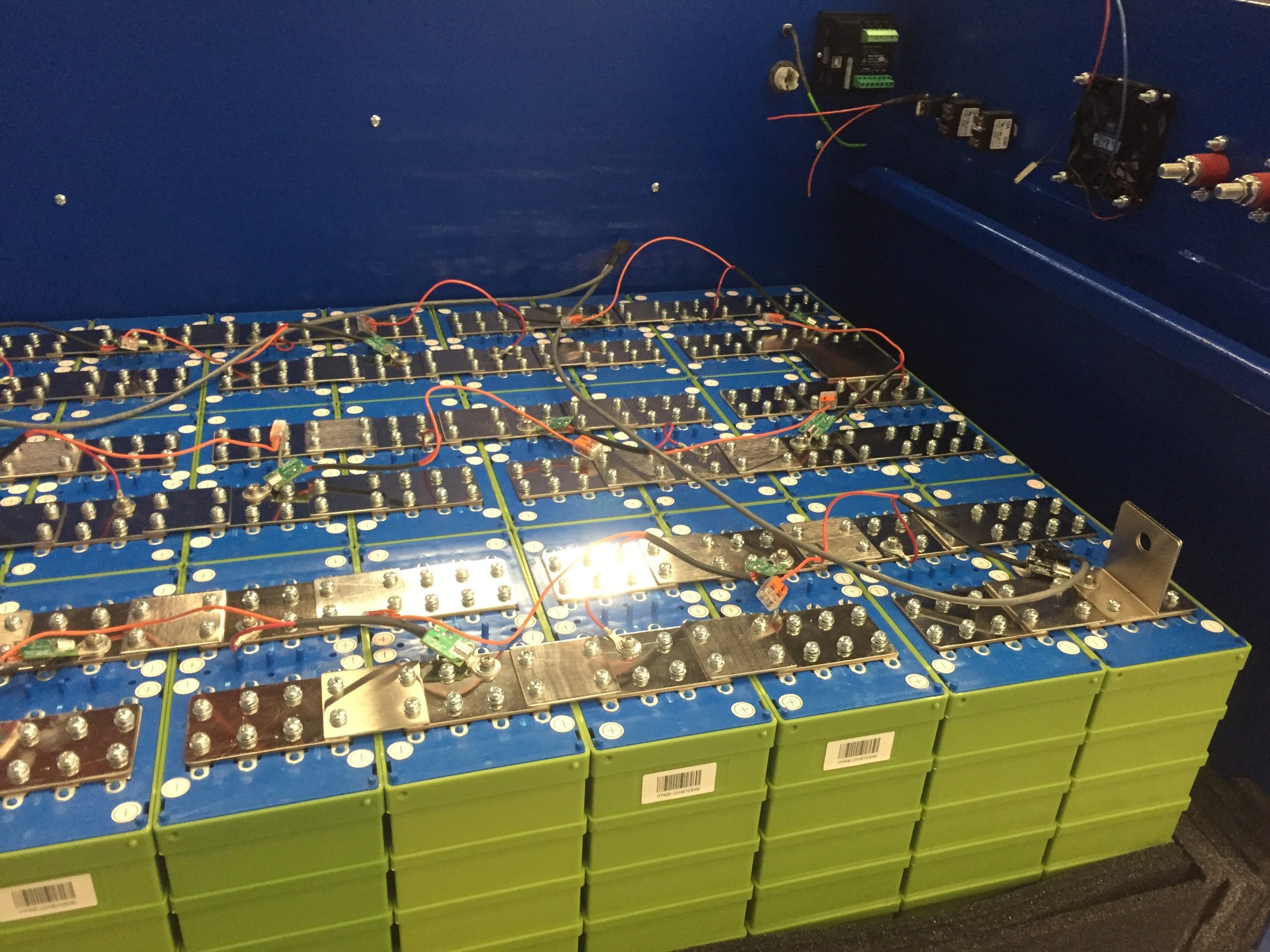 A bank of prismatic lithium iron phosphate cells linked by busbars and balance leads with a battery management board behind