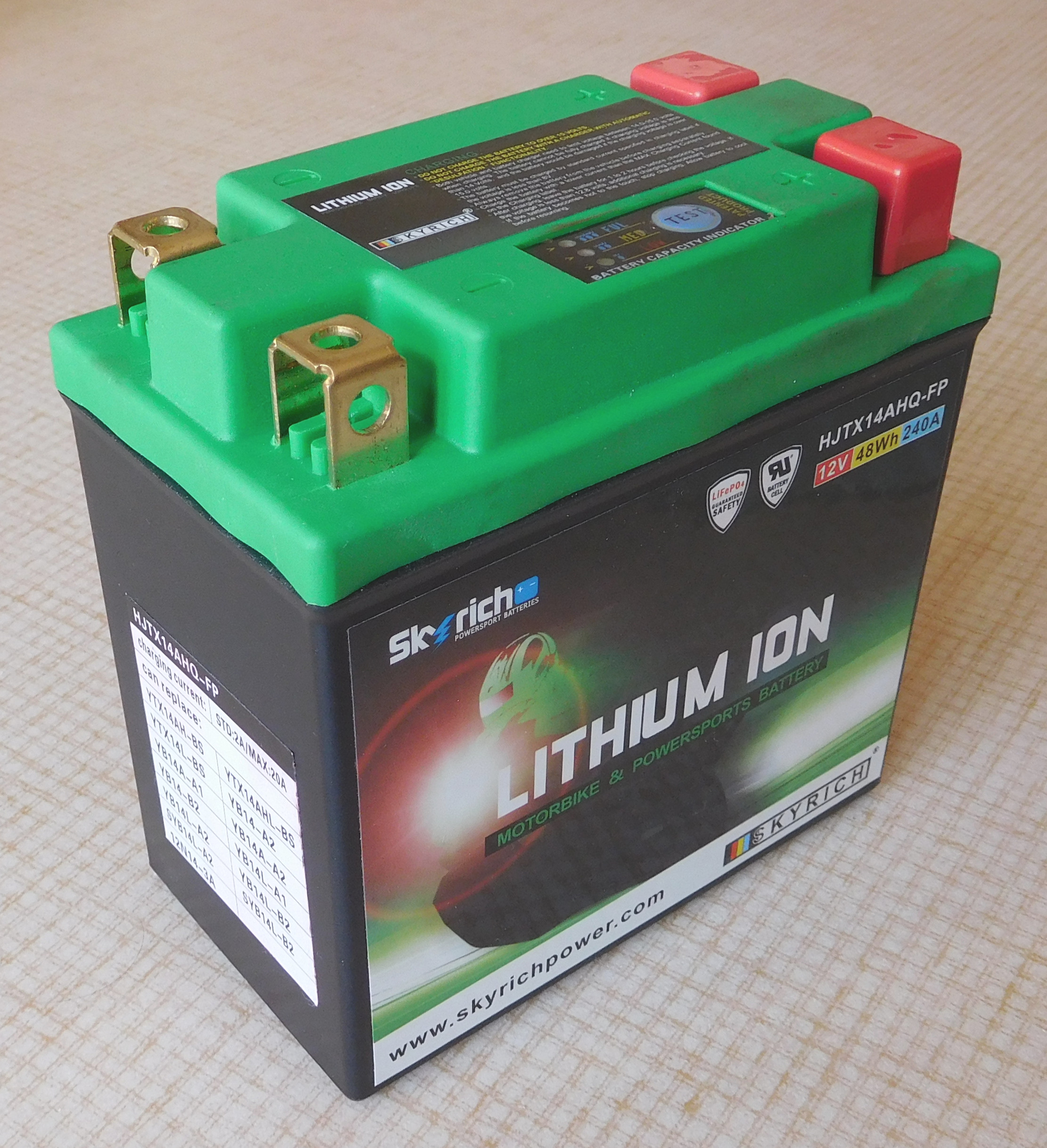 A green 12-volt lithium iron phosphate battery with brass terminals and a small charge gauge on top