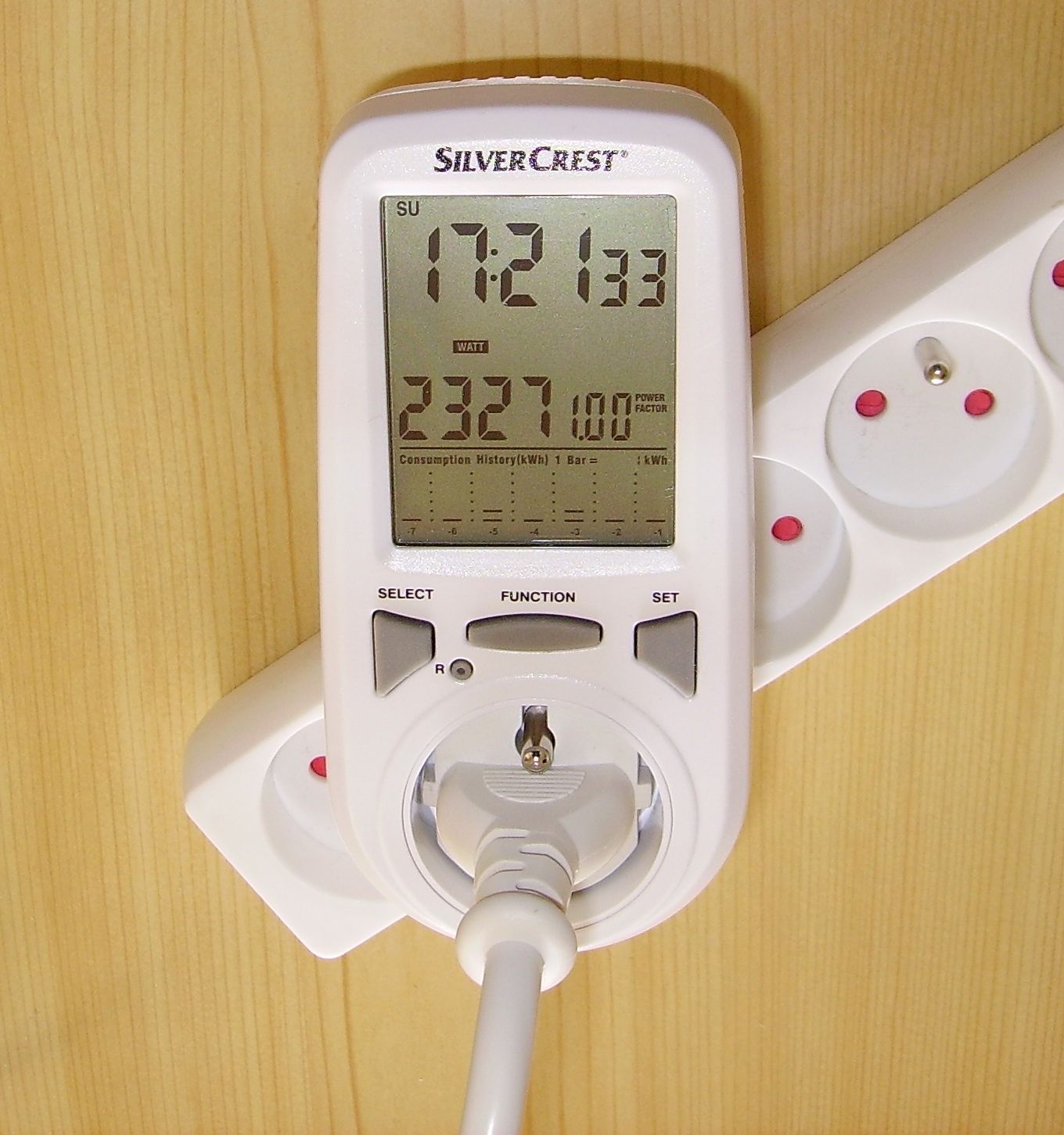 A plug-in mains energy monitor plugged into a wall socket, showing a digital reading