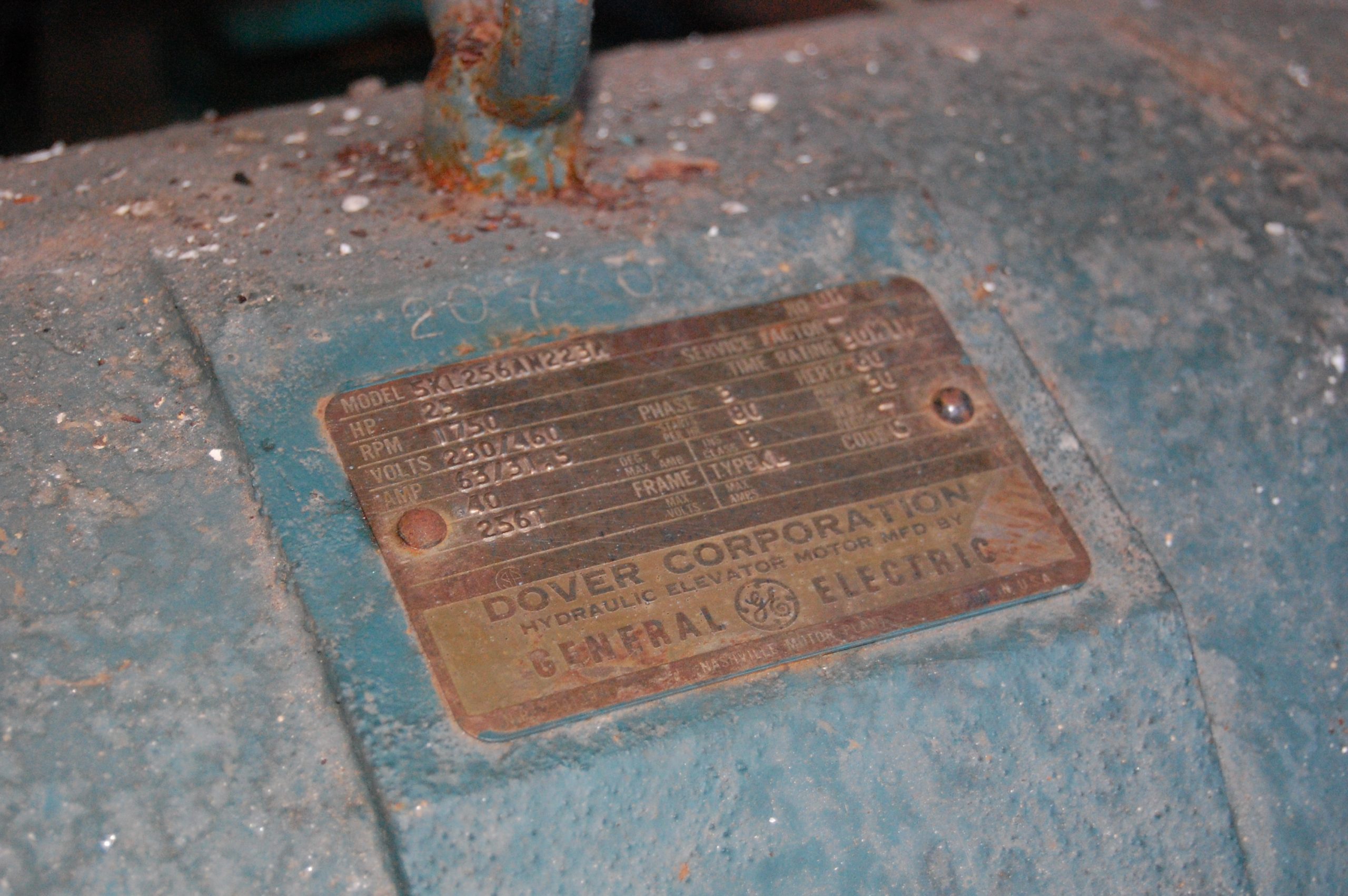 A rusted nameplate on an electric motor showing horsepower, voltage, amps and a NEMA code letter