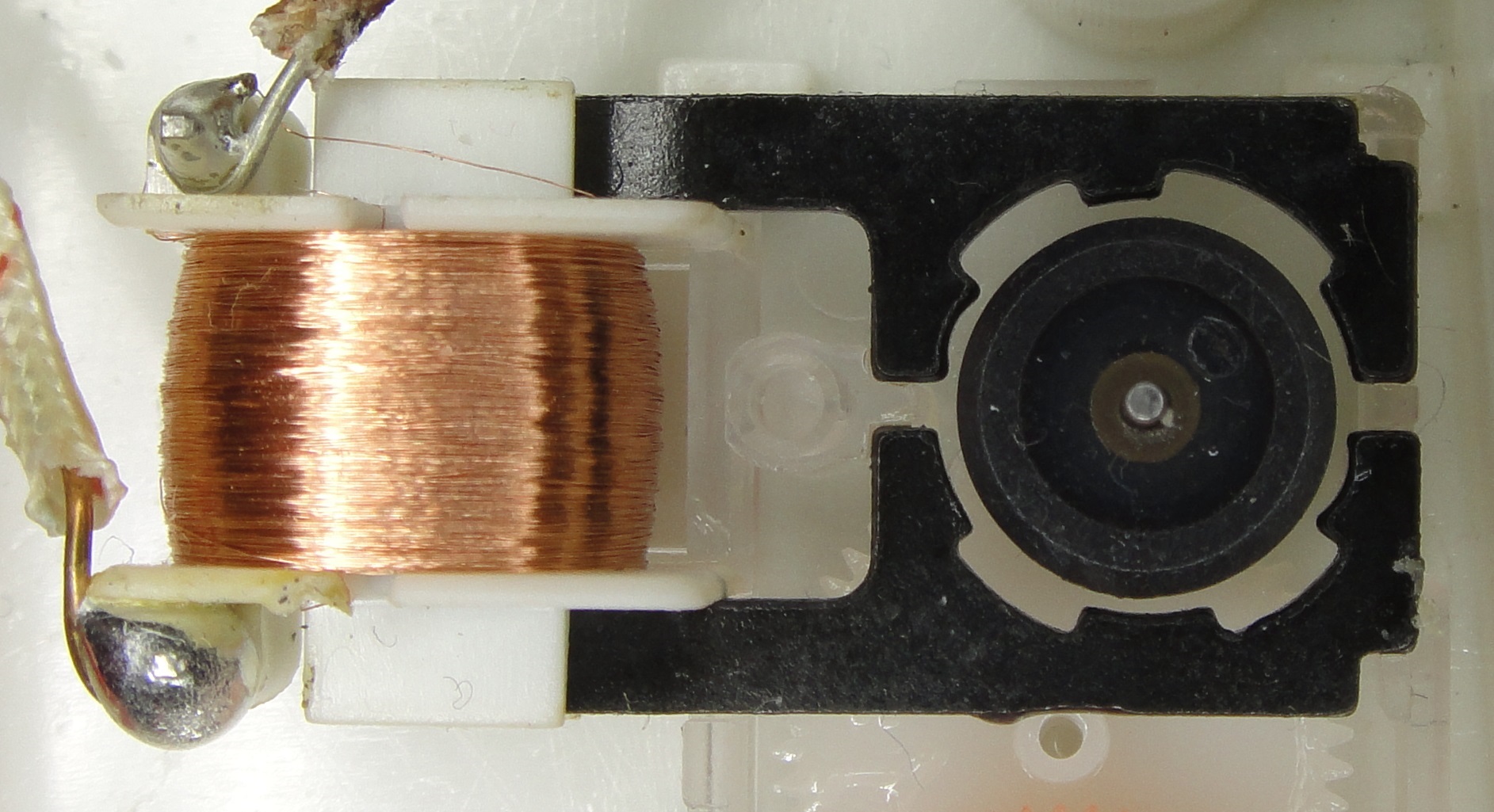 A single-phase synchronous clock motor with its cover removed, showing a copper coil and a rotor