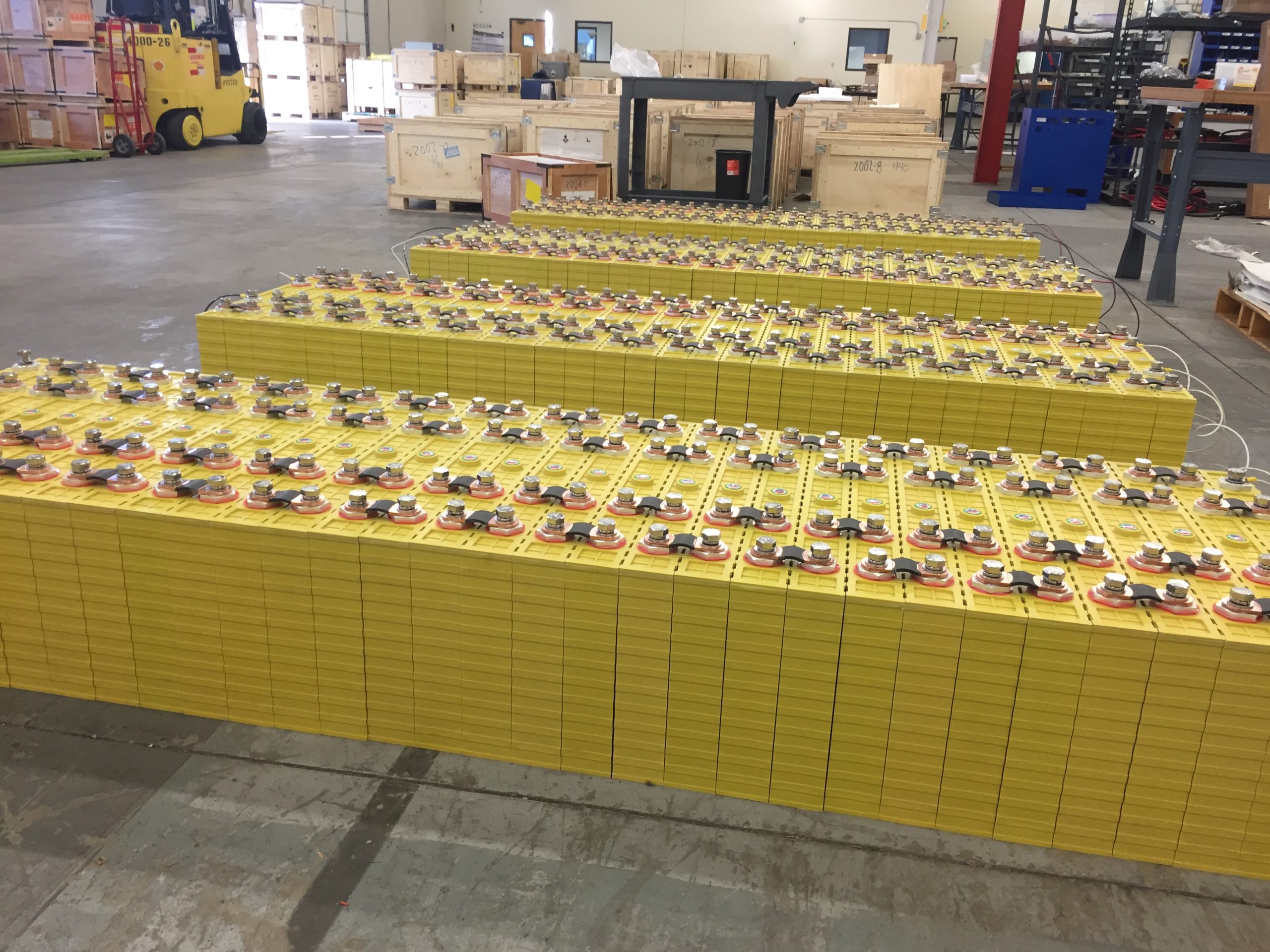 Rows of large yellow prismatic LiFePO4 cells wired in series with bus bars in a warehouse