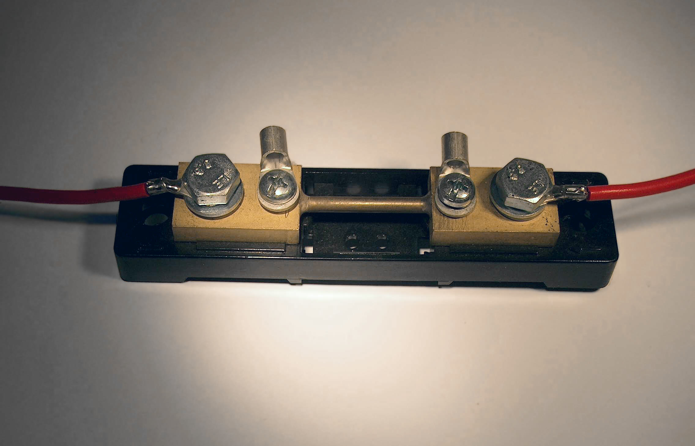 A 50-amp current shunt with two bolt terminals and two small sense terminals, red battery leads attached