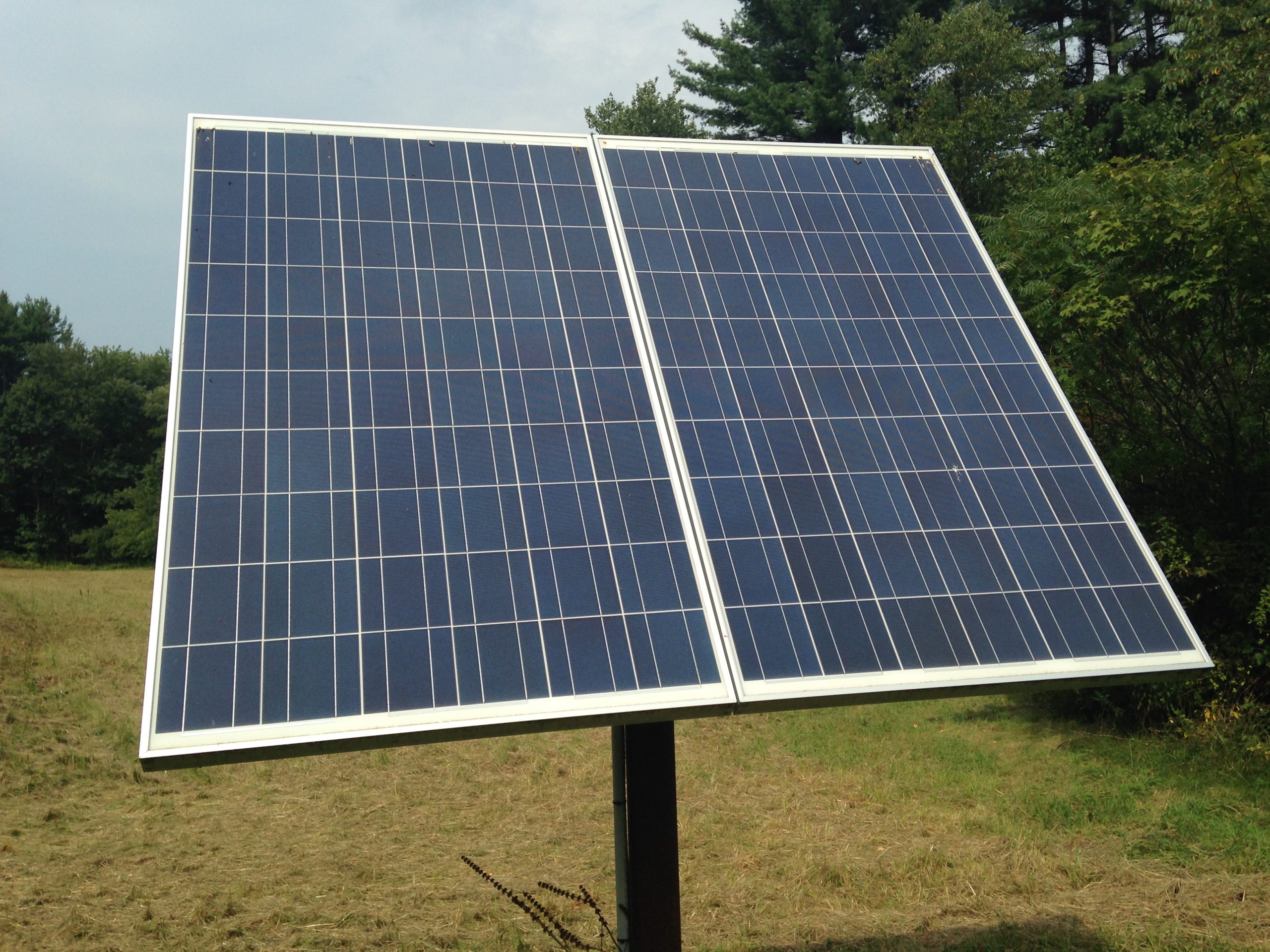 Two polycrystalline solar panels on a pole mount outdoors under a hazy sky