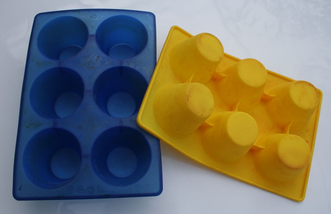 Two flexible silicone six-cup muffin baking forms, one blue and upright, one yellow and flipped inside out to show how it bends