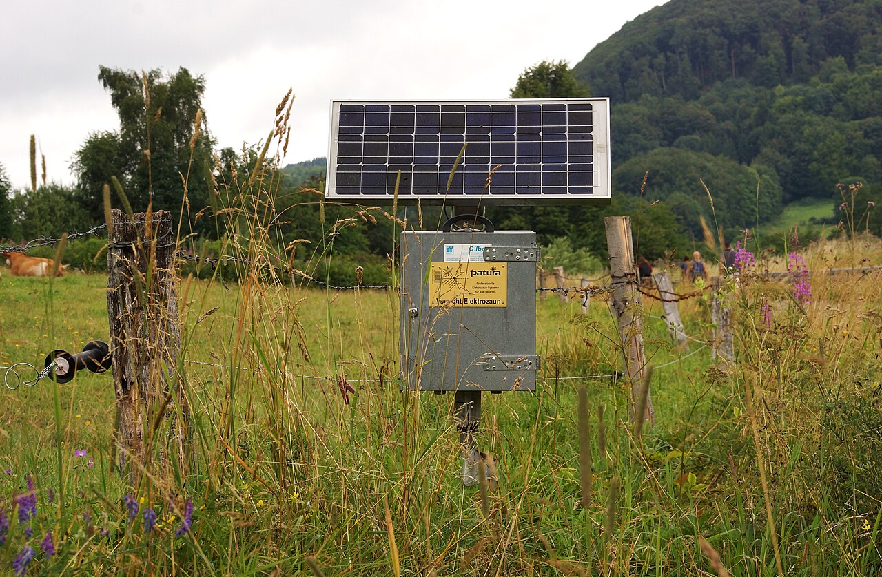 Solar fence energizer station with panel and battery box, front view on pasture
