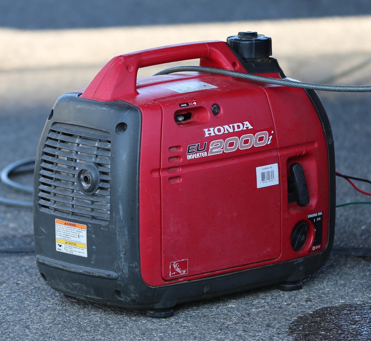 A red Honda EU2000i portable inverter generator on pavement, with its INVERTER model badge visible