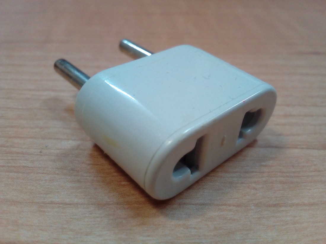 A white travel adapter with two round European pins and American flat-blade slots, no earth contact