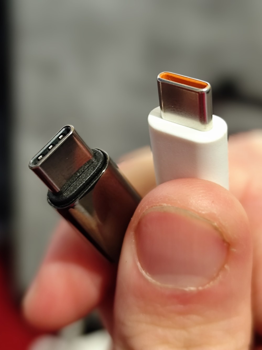 Two USB-C plugs held in fingers, one black and one white, outwardly identical apart from a coloured inner tongue