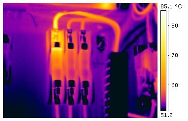 Infrared thermogram of an industrial electrical terminal block with several bright yellow hot spots against a cooler purple background, temperature scale from 51 to 85 degrees