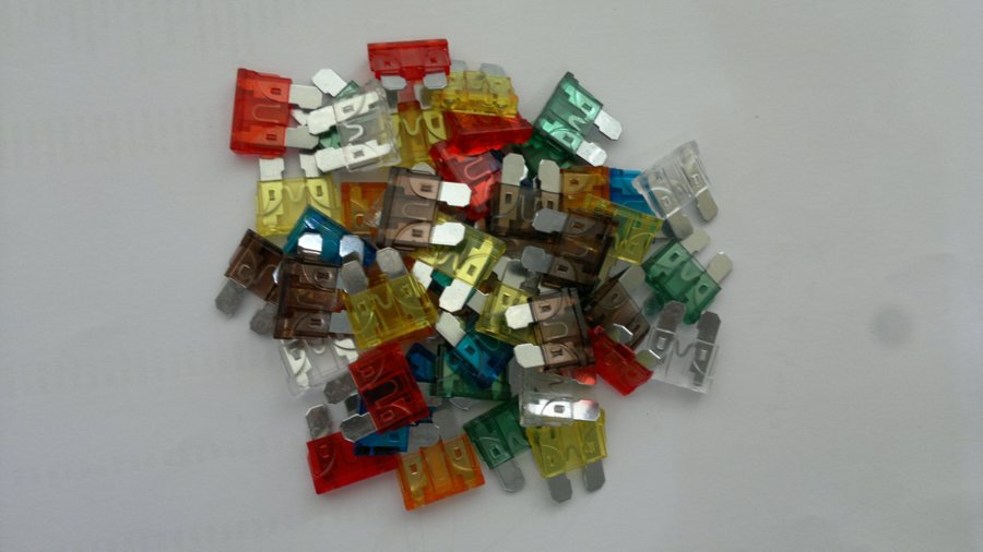 A pile of automotive ATO blade fuses in many colours, each colour marking a different amp rating