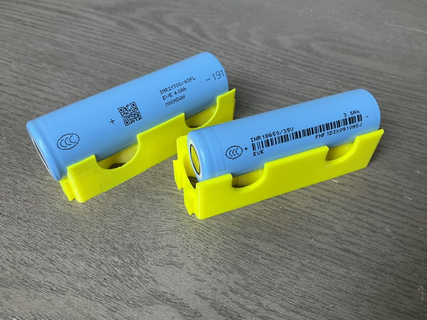 Two cylindrical lithium cells, a 21700 and an 18650, in yellow holders, their model and capacity markings visible