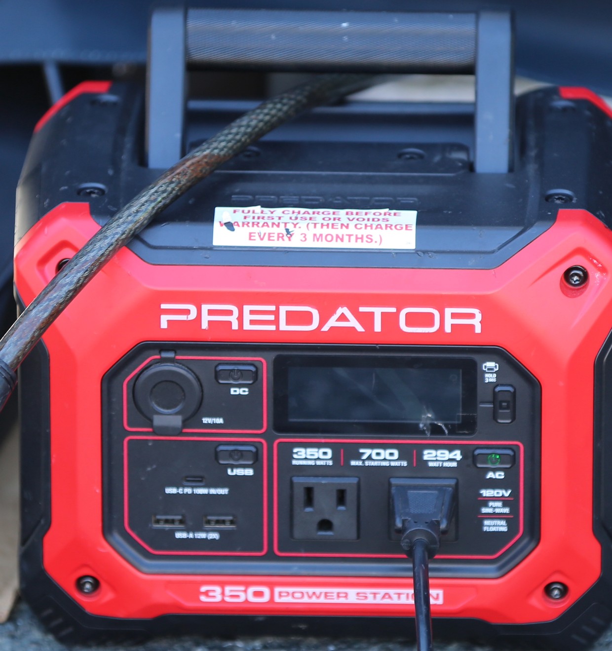 Front of a red portable power station with a factory sticker reading fully charge before first use or voids warranty, then charge every three months, above a panel marked 350 running watts and 294 watt hours