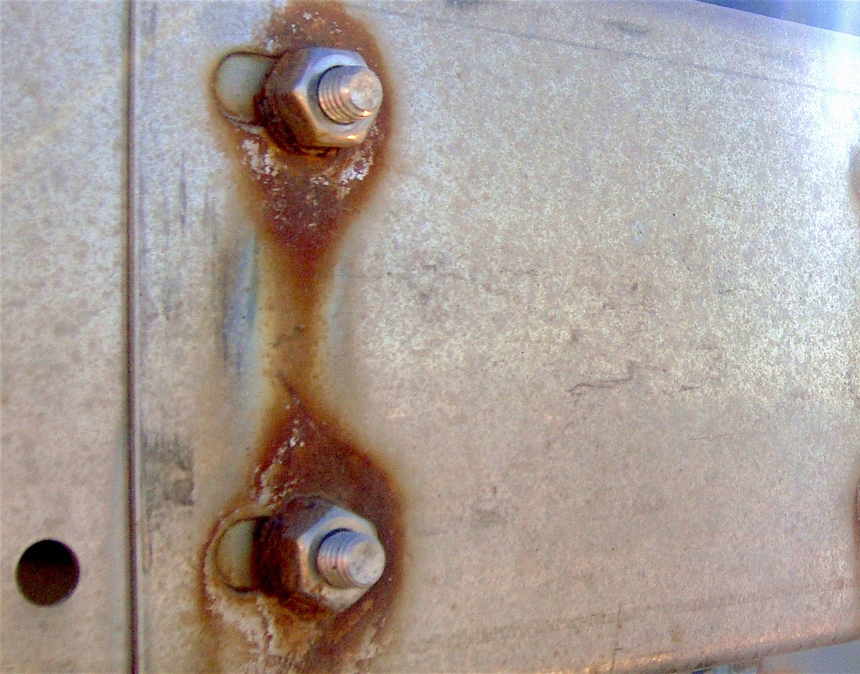 Steel plate with rust haloes spreading from each bolt where fasteners pass through it