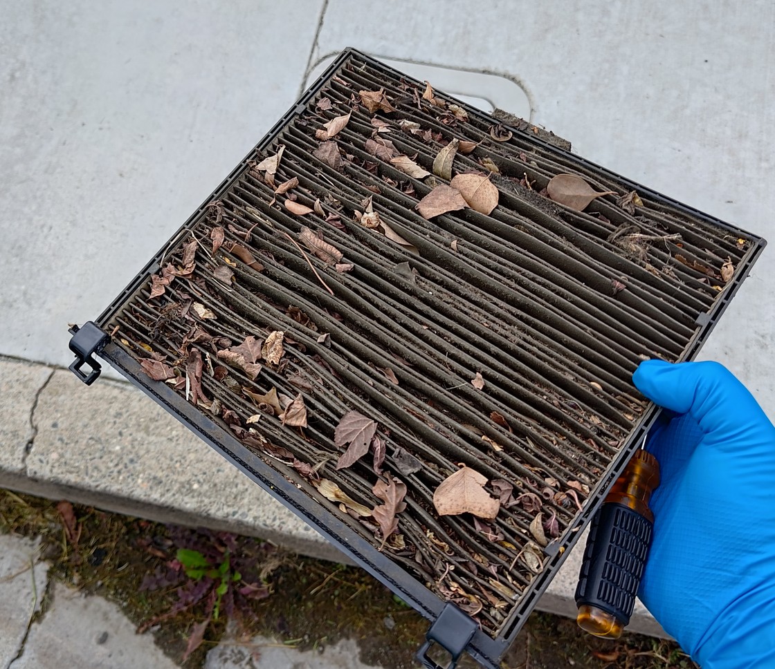 A pleated cabin air filter loaded with leaves and dirt, held in a gloved hand