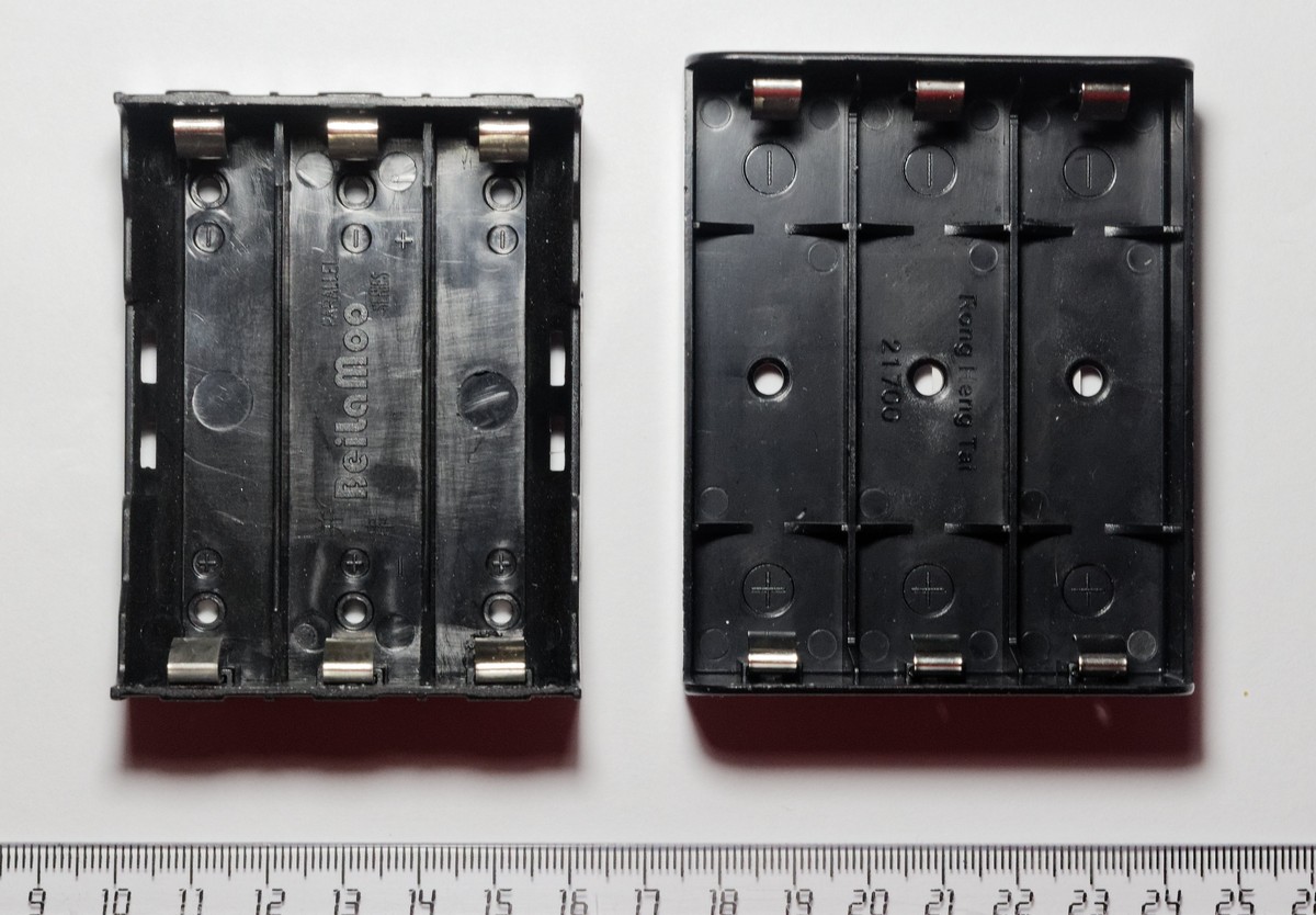 Two three-cell battery holders side by side above a centimetre ruler, one sized for 18650 cells and one for 21700 cells