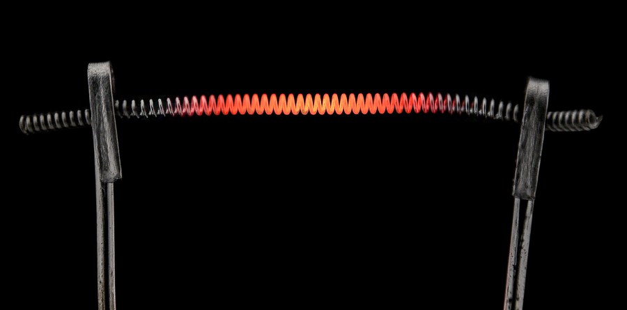 A coiled tungsten lamp filament glowing orange on its support wires against a black background