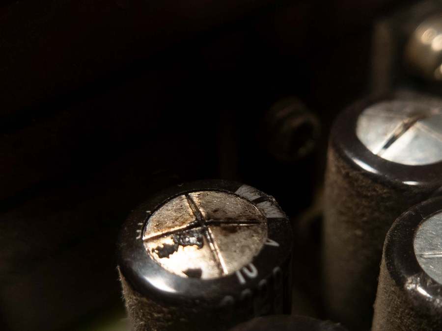 Close-up of aluminium electrolytic capacitors on a circuit board, one of them vented with dried residue on its scored top