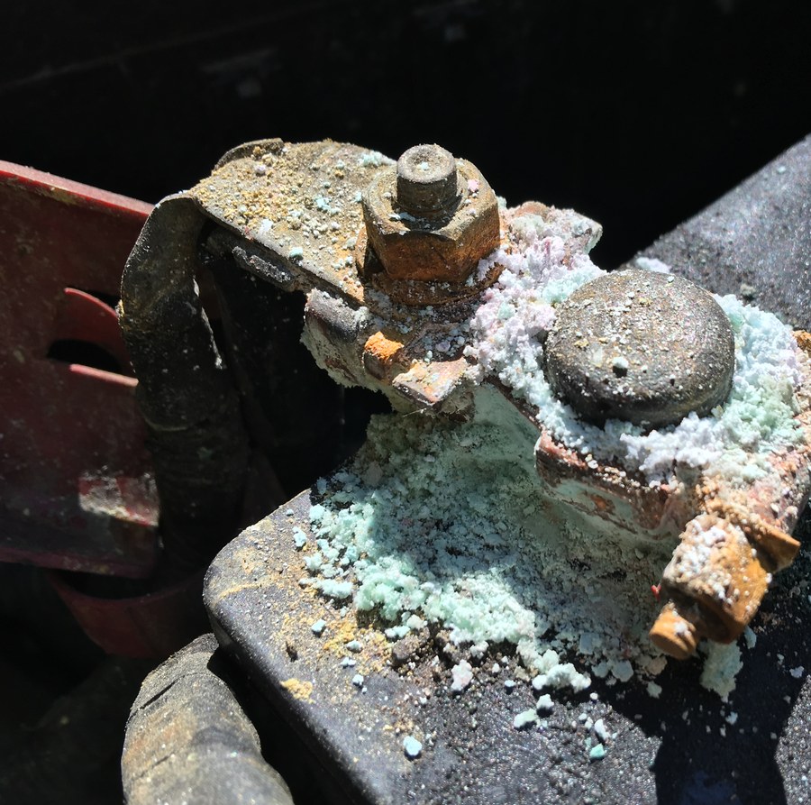 A battery terminal clamp buried in green and white corrosion crystals