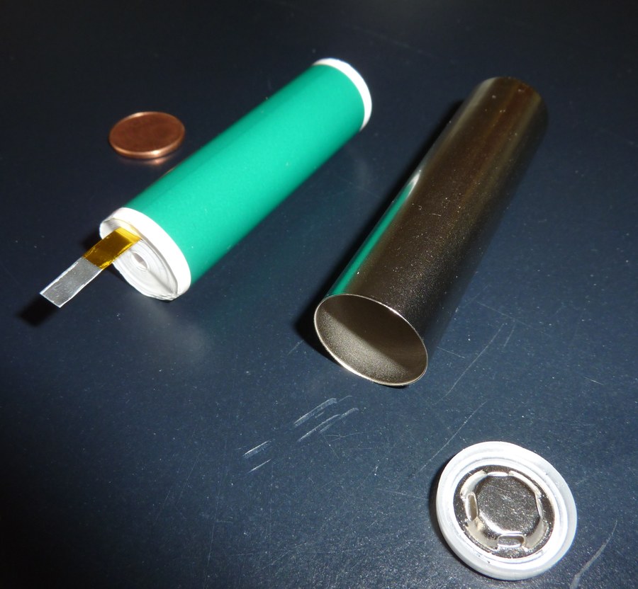 A dismantled cylindrical lithium ion cell showing the wound electrode assembly, the empty steel can and the cap with its vent