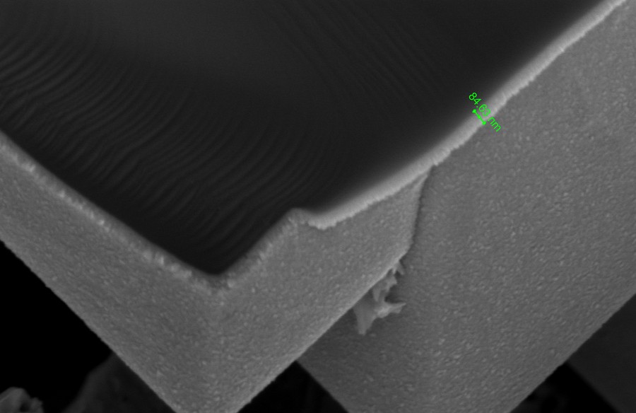 Scanning electron micrograph of a coated solar cell surface in cross-section, showing a thin conformal film over the textured silicon with a measurement marker on the film thickness